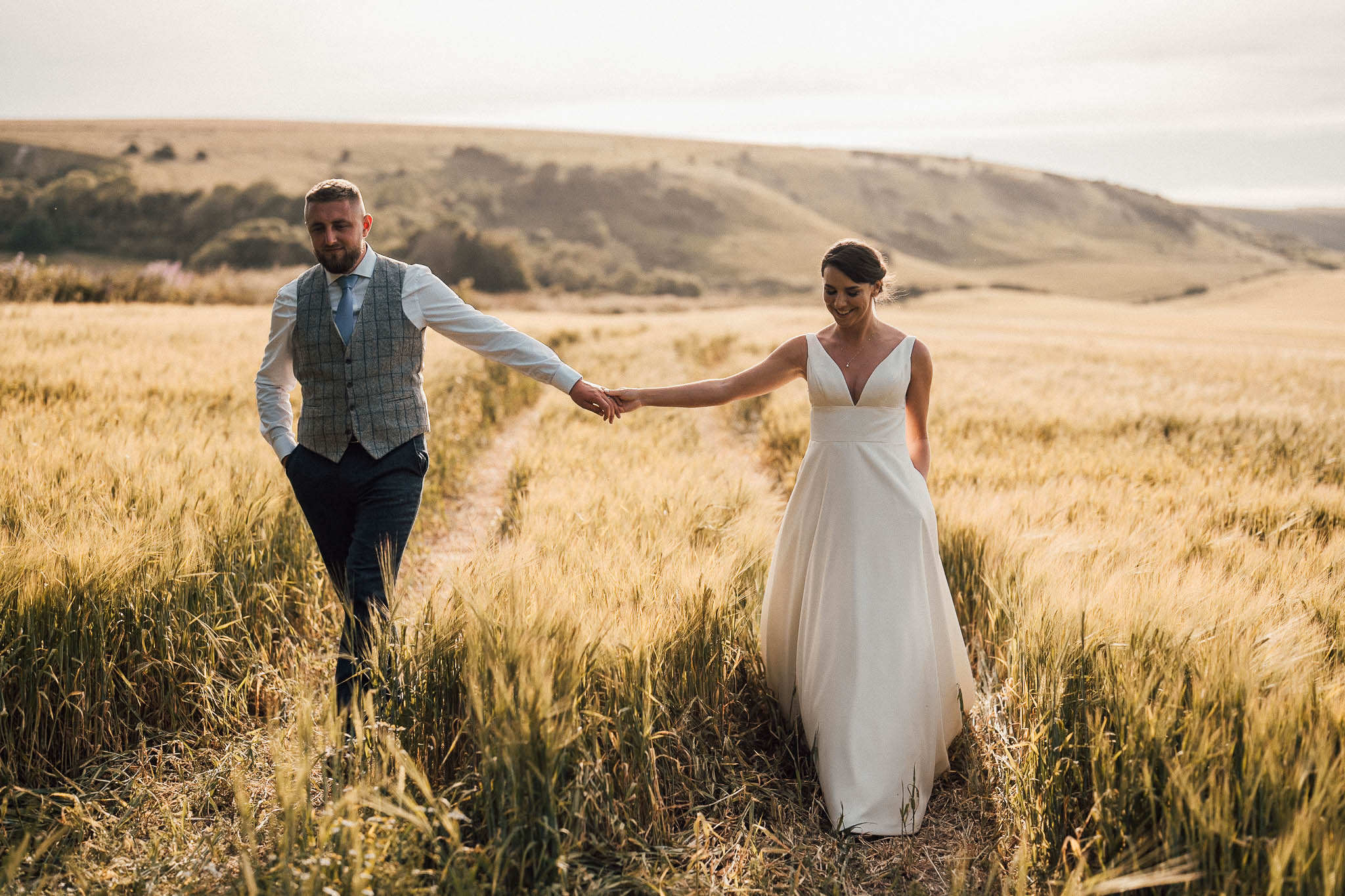 South Downs National Park as the backdrop to couples photo walking through a field next to Wedding Venue Alfriston Gardens