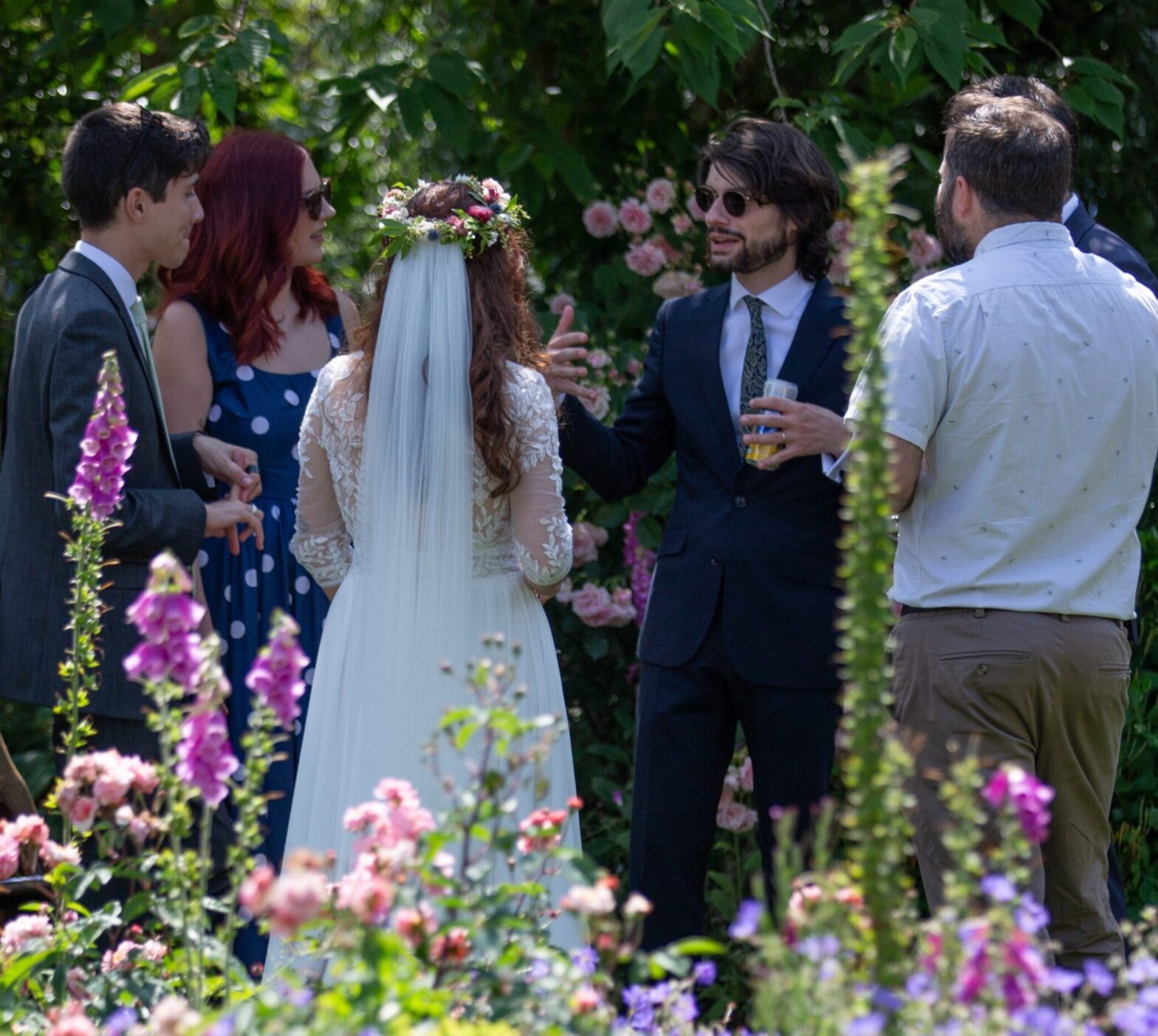 Bride and groom stand with guests in the grounds of Alfriston Gardens during a weekday wedding reception drinks in the summer